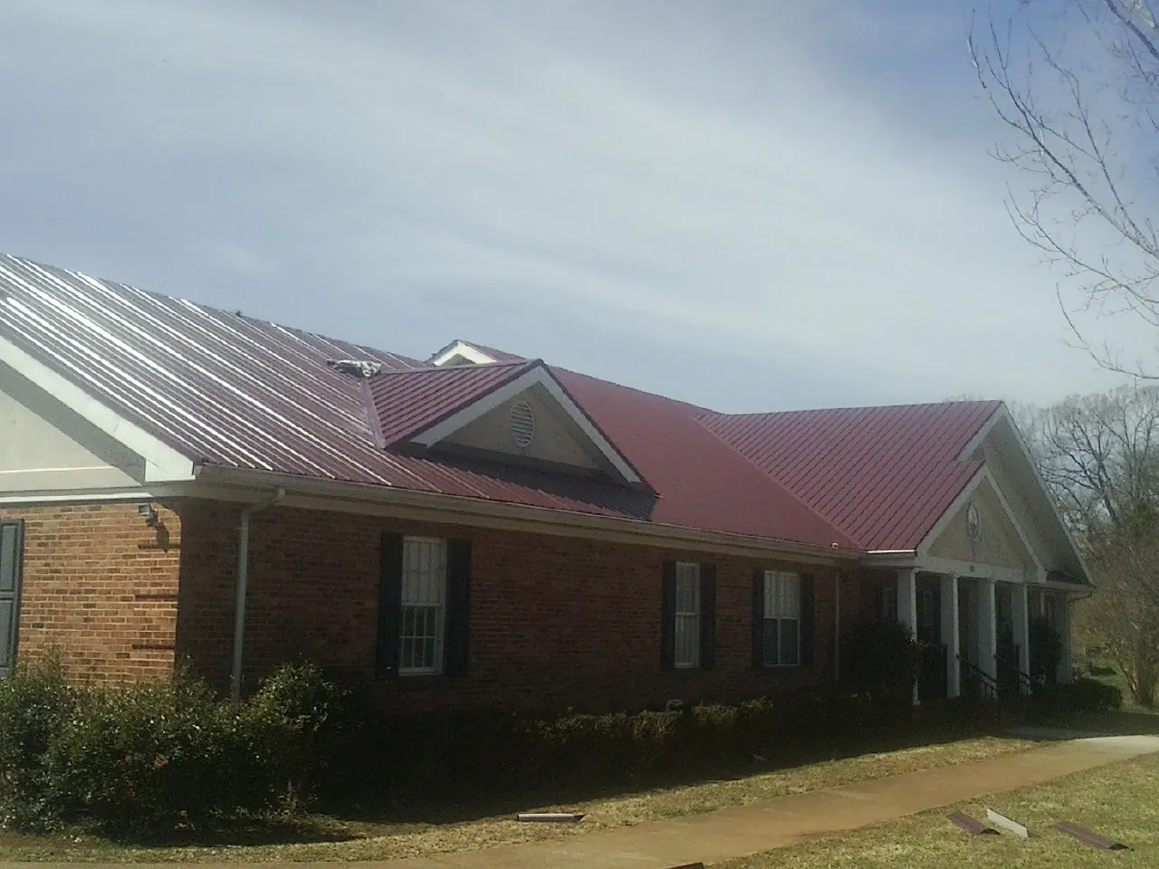 Red metal roof with gabled entries on a long brick building, from a Hail Damage Roof Repair job in Hamtramck