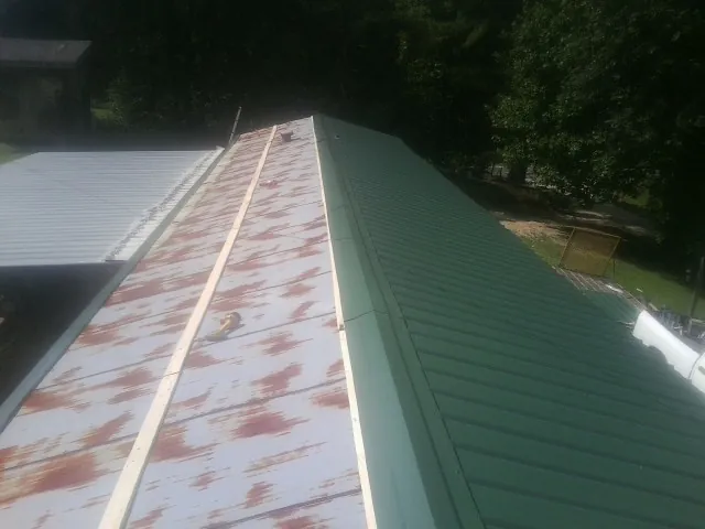 Old rusted panels beside newly installed green metal roofing — Wind Damage Roof Repair by Roofing Brothers in Hamtramck