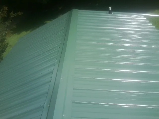 New green metal panels meeting at the ridge of a roof — Flat Roof Repair work by our crew in Hamtramck