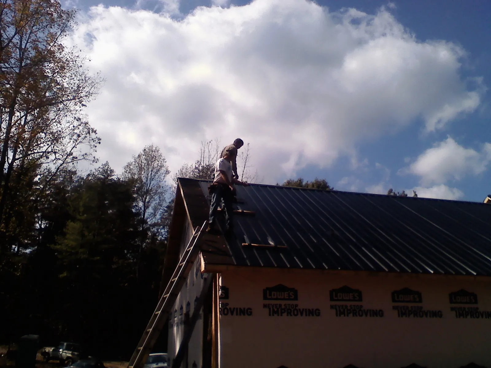 Roofer fastening dark metal panels high against a cloudy sky, from a Roof Inspection job in Hamtramck